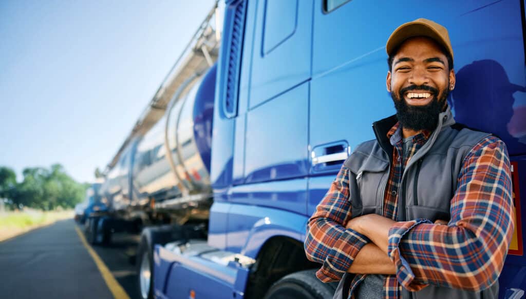 Cheerful truck driver leaning on his vehicle and looking at camera.